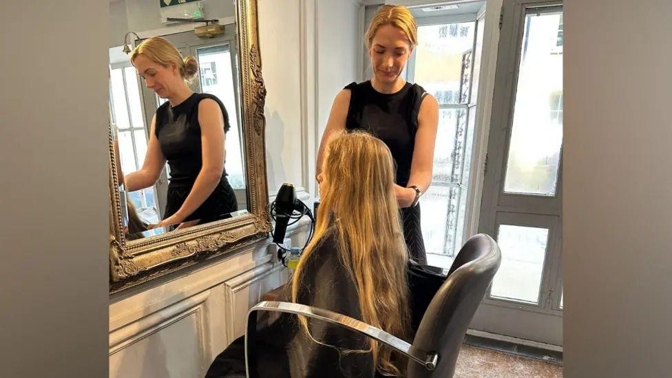 blonde boy with long hair getting a haircut at a hairdresser.