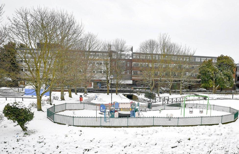 A snow covered playground next to a building block.