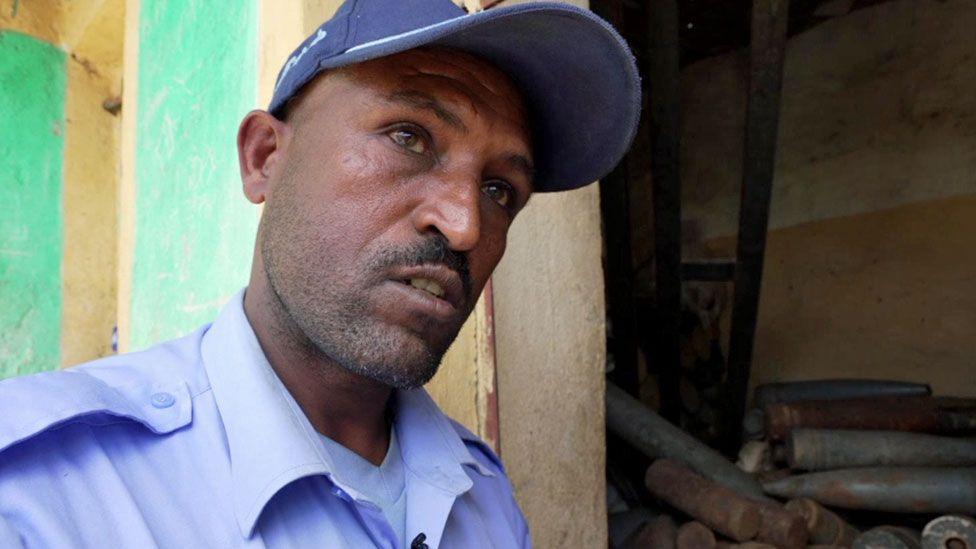 Police commander Hadush Gebremedhin in his blue uniform seen with a room full of weapons like mortar shells behind him 