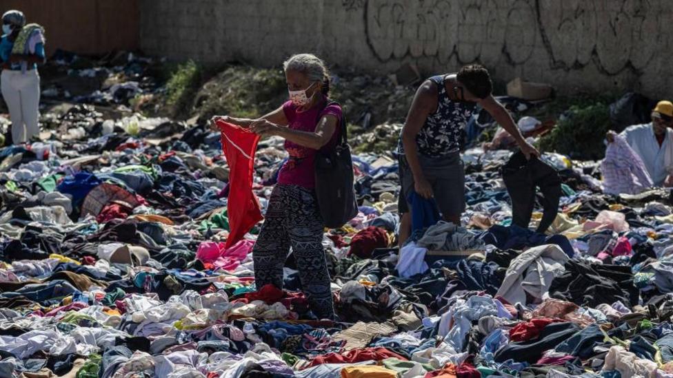 Four people looking through donated clothing which is piled all around them