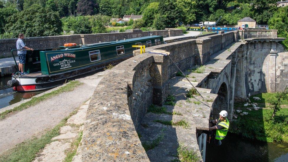 a canal boat using the Dundas aqueduct while stonemasons carry out repairs to detailed mouldings