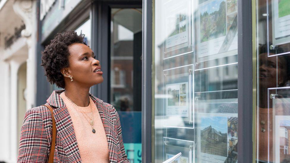 Woman looking at pictures of properties in the window of an estate agents