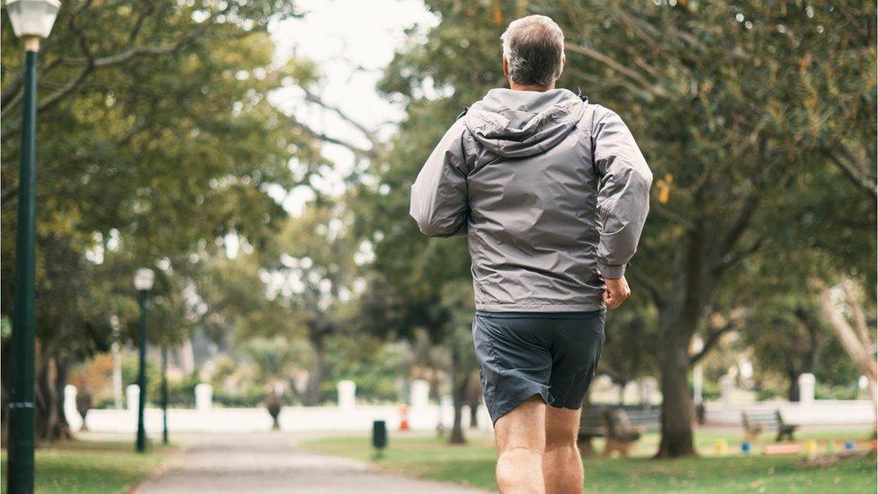 Anonymous man running through a park from behind