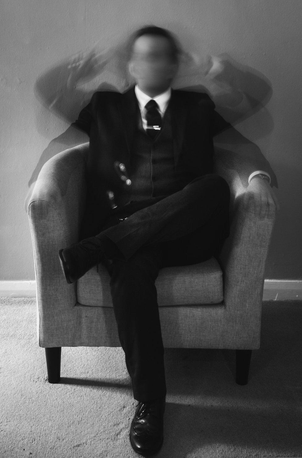 A blurred photo of a man sitting in a chair waving his arms around