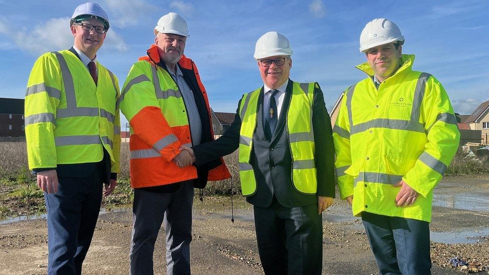 Four men wearing Hi-Vis jackets and helmets while standing on a construction site