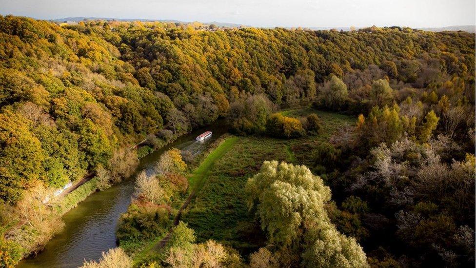 A river boats makes its way through autumnal trees surrounding the River Avon as it flows through Conham and St Annes in east Bristol