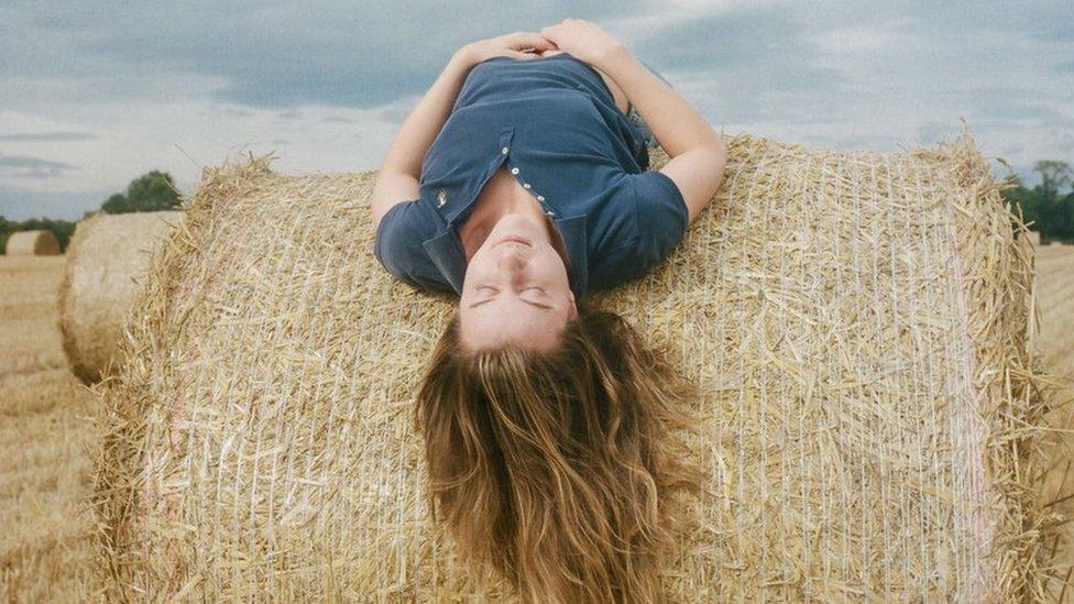 Poppy, a vet and farmer's daughter, lies across a hay stack at her home farm near Foulden in the Scottish Borders