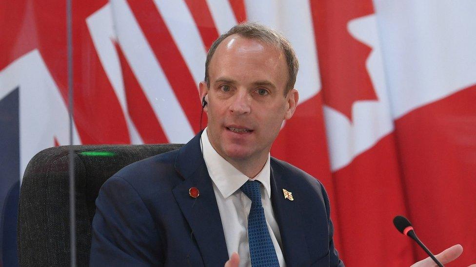 Dominic Raab delivers an address seated before a range of flags