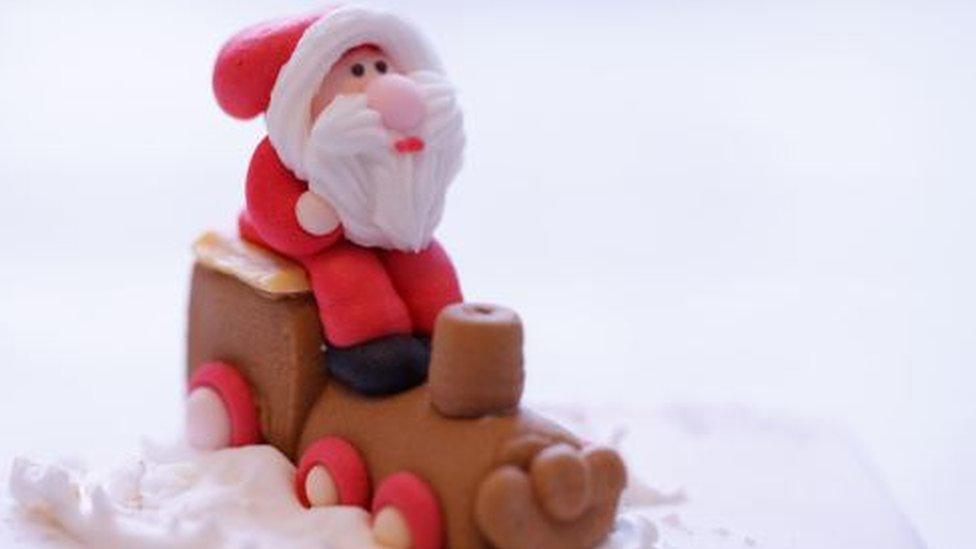 A sugar figurine of Father Christmas sitting on a train on a Christmas cake