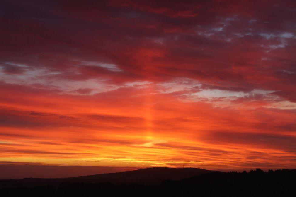 Orange glow in sky at sunrise over a dark morning hillside.