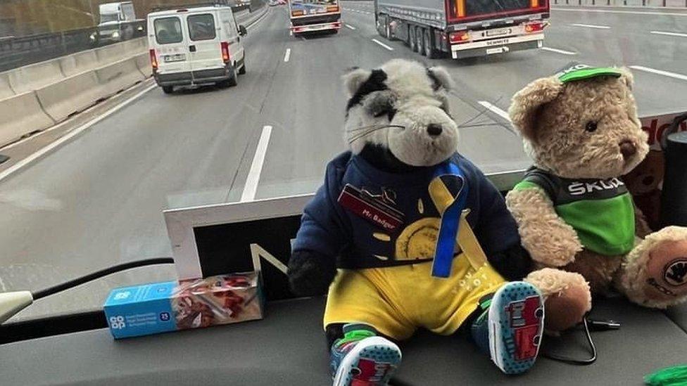 Two teddies on the dashboard of the bus as it's being driven on the road