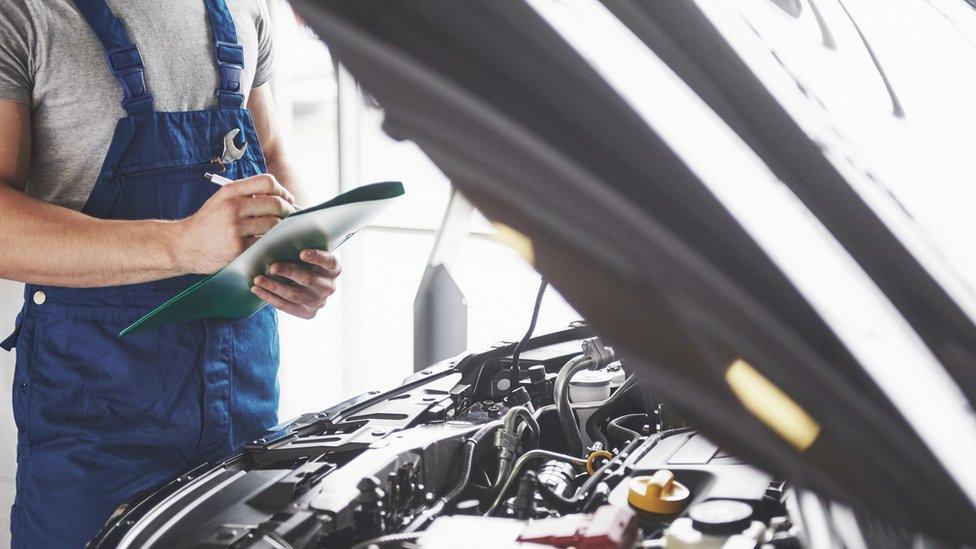 Portrait of a mechanic at work in his garage - car service, repair, maintenance and people concept - stock photo