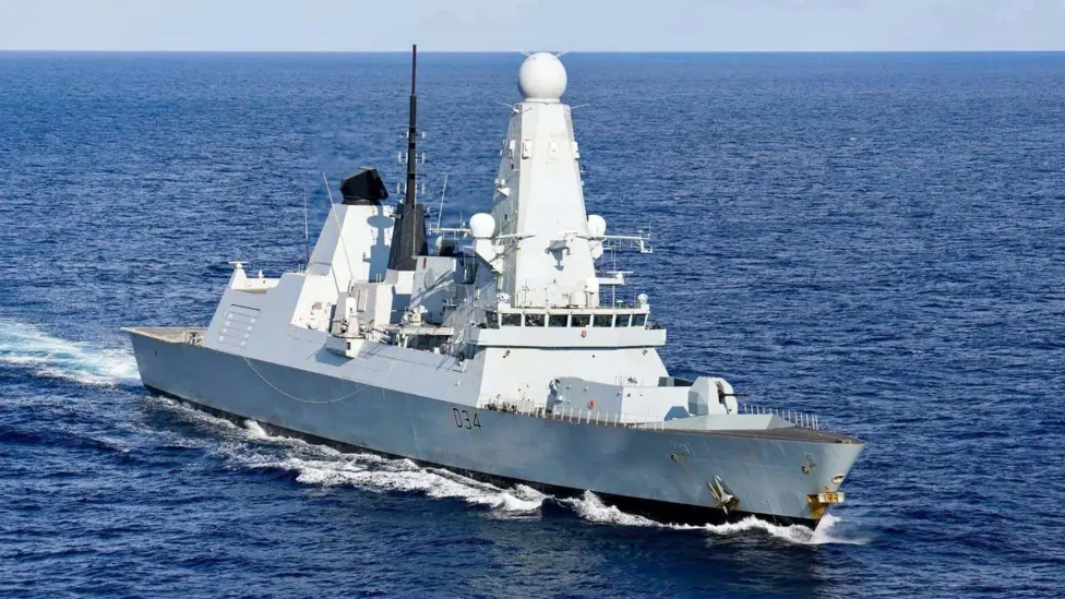 HMS Diamond is a large grey warship and is sailing through richly blue sea water.