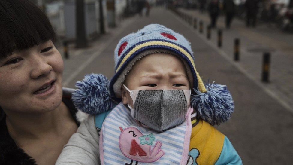 A Chinese girl wears a mask as she is held by her mother during a day of heavy smog in Beijing, China