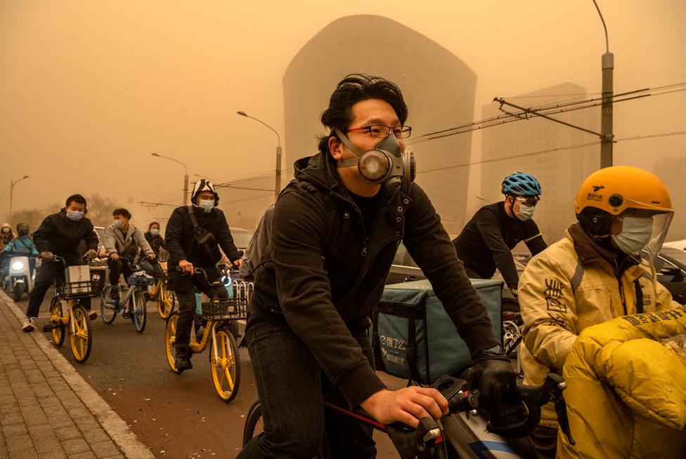 People wear protective masks as they cycle during a sandstorm on 15 March 2021 in Beijing