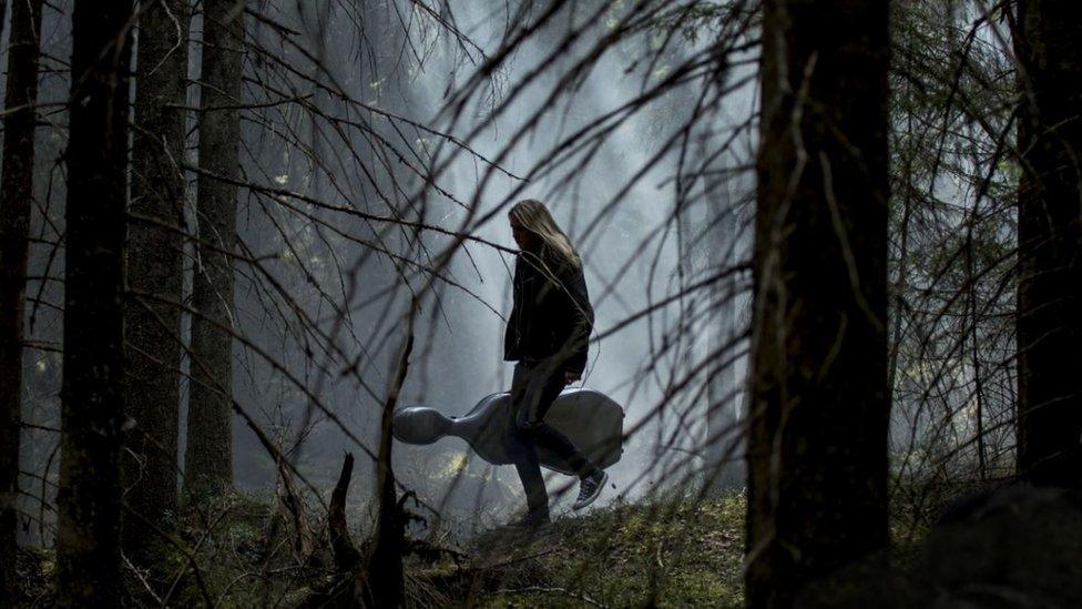 Girl calmly walking through a Finnish forest in the dark with her instrument