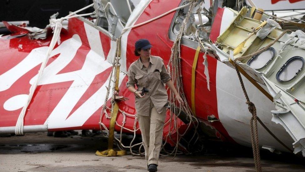 An Airbus investigator walks near part of the tail of the AirAsia plane