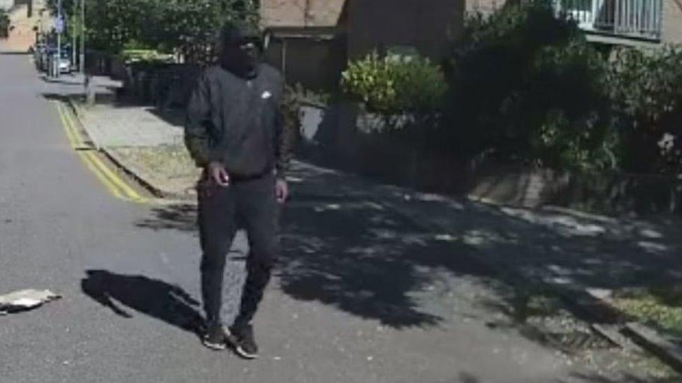 CCTV image of one of the men wearing a face covering and a hooded jacket with a white logo.