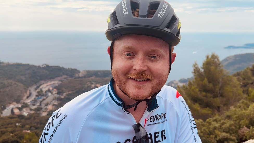 Travis Frain wearing a cycling helmet with French mountain views in the background