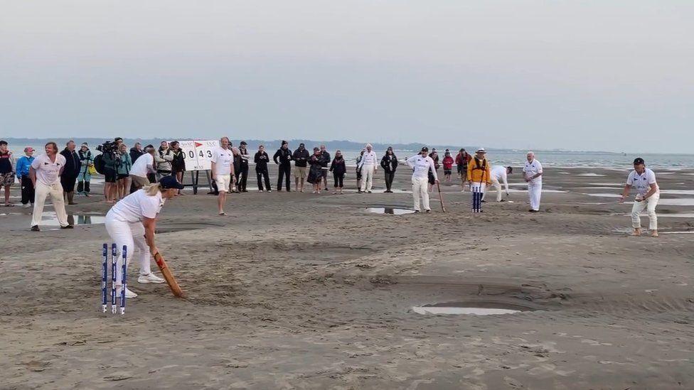 Cricket players on the crease ready to bowl and bat with others looking on