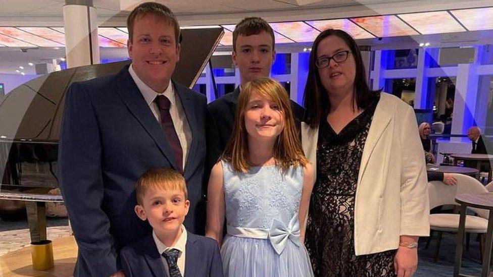 family of five - a wife, husband, two boys and a girl - stand together in formal dress