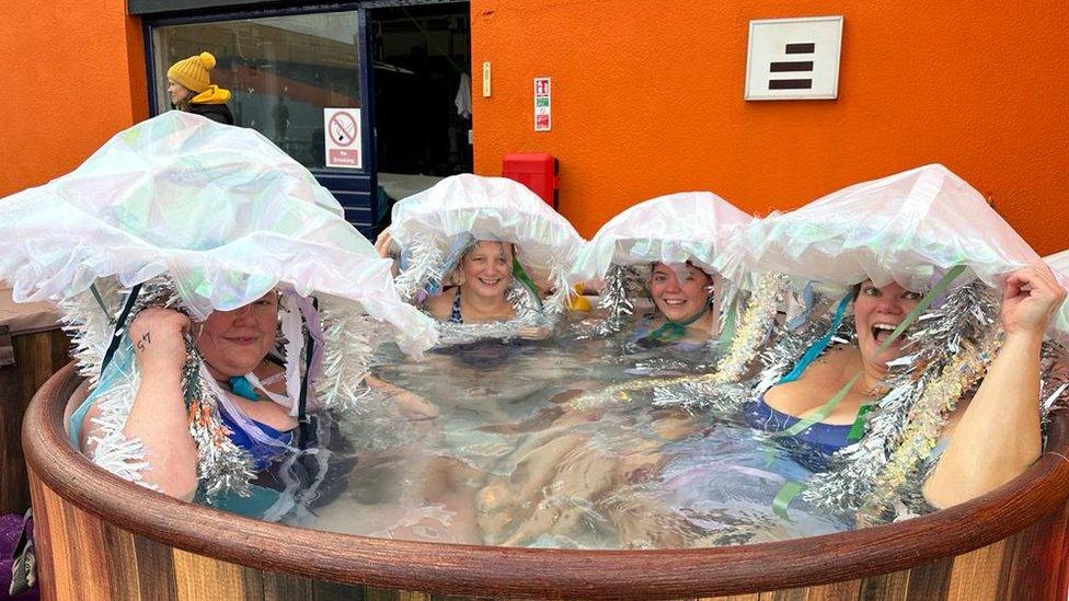 Four women in a hot tub wearing jellyfish costumes with tinsel attached