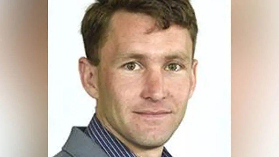 Head and shoulders image of Tom Pickup. He has short brown hair, brown eyes and is wearing a grey suit jackets and a navy blue shirt with a fine white stripe