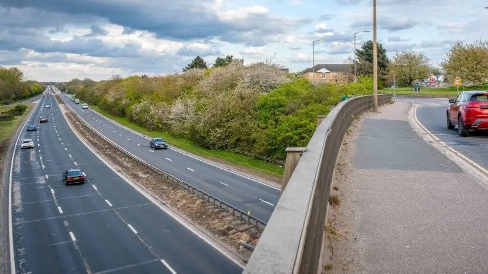 A major road with five lanes runs under a road bridge slip road.