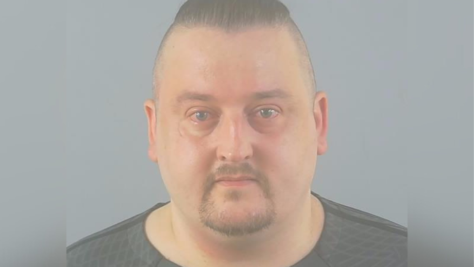 Ryan Wheatley custody picture - looking directly into the camera. He has short hair on top and shaven round the sides. He also has a goatee beard.