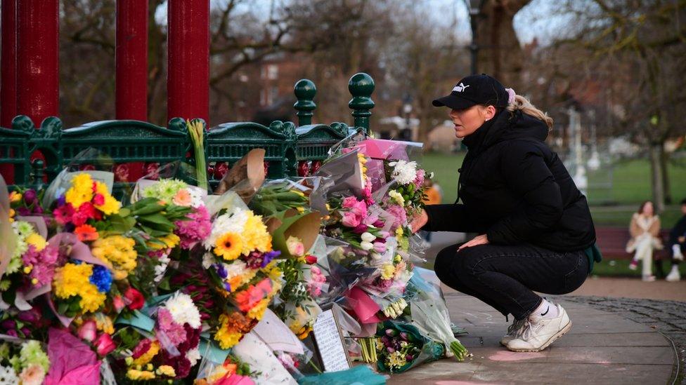 A woman leaves flowers at the bandstand on Clapham Common