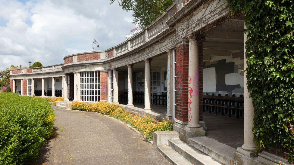 Sun Shelter, Cliff Gardens, Westcliff Parade, Westcliff-on-Sea. The single-storey  shelter is curving away and has glazed panels, columns and balustrade above. In front of it is a pavement. 