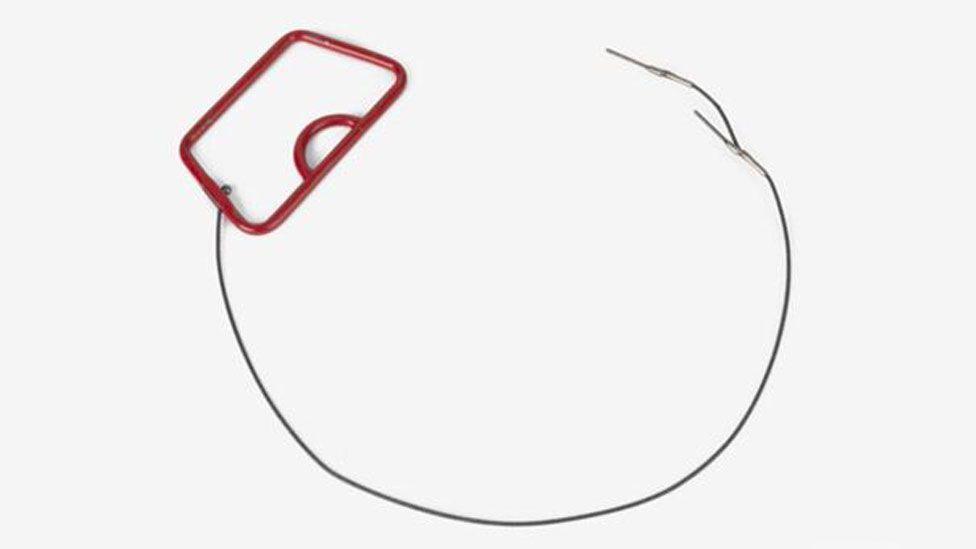 A World War Two US parachute rip cord. Top left is a red rectangle and from it is a lengthy of cloth shaped into a near-circle. 