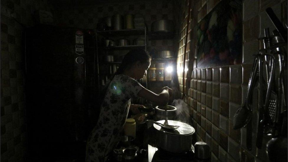 A woman uses her mobile phone torch as she cooks food inside her kitchen during a power outage in Mumbai, India, October 12, 2020.