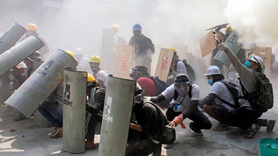 Protesters take cover as they clash with riot police officers during a protest against the military coup in Yangon