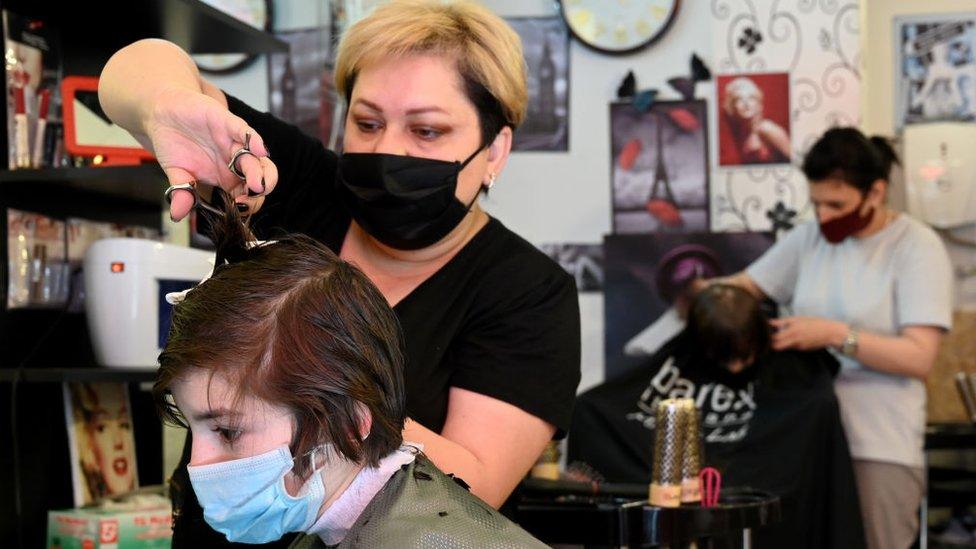 A hairdresser wearing a face mask cuts the hair of a client at a hairdressing salon in Georgia