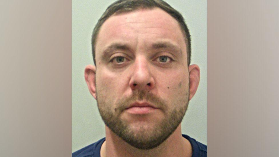 A police mugshot of Grant Eddleston, who has short brown hair and stubble, looking into the camera with a blank expression