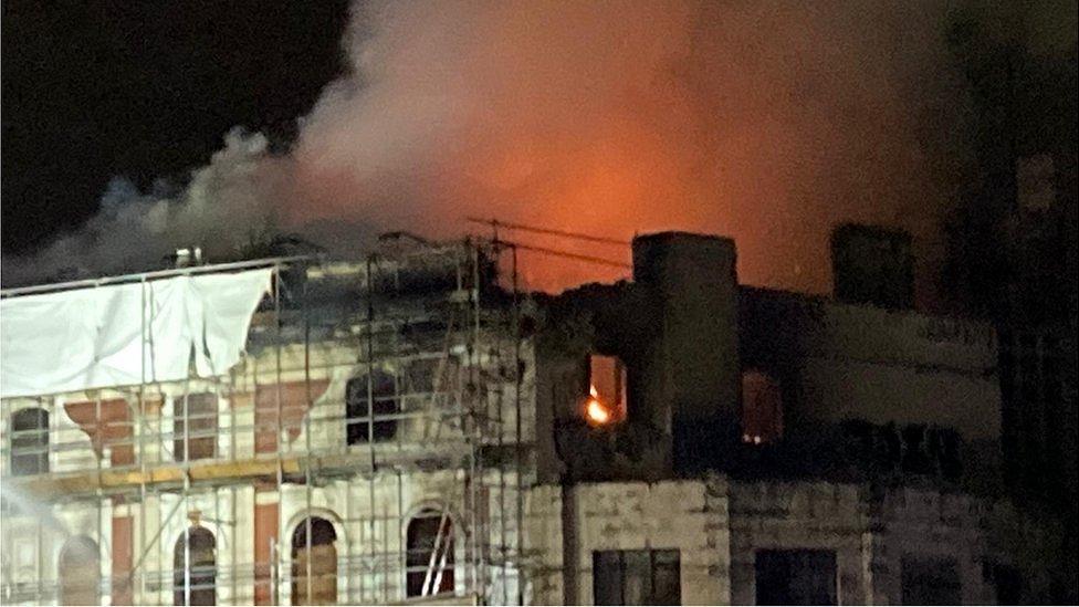 Red and orange flames near the roof of a building. Smoke is rising into the night sky.