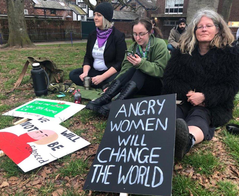 Three women sitting with protest signs