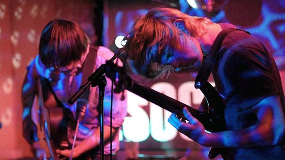 Ollie and Michael in an older picture, playing in their band ute. They are in the moment, heads down, as they play their guitars with intensity.