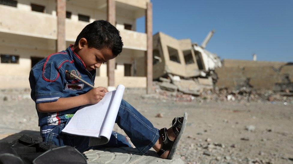 A Yemeni boy school writes as he sits outside a school which was damaged in an air strike in the southern Yemeni city of Taiz