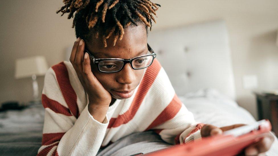 Teenager looking at tablet computer on bed