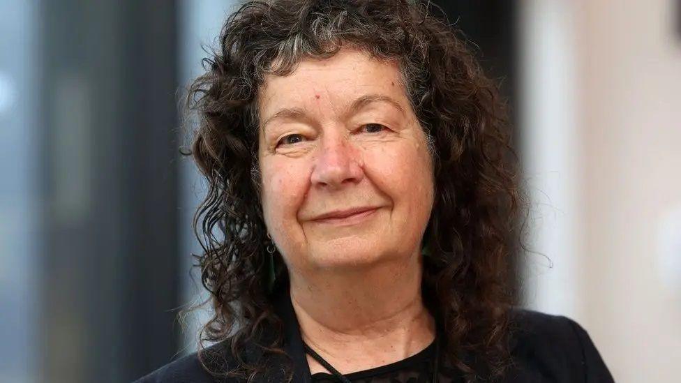 A woman with mid-length curly brown hair smiling at the camera