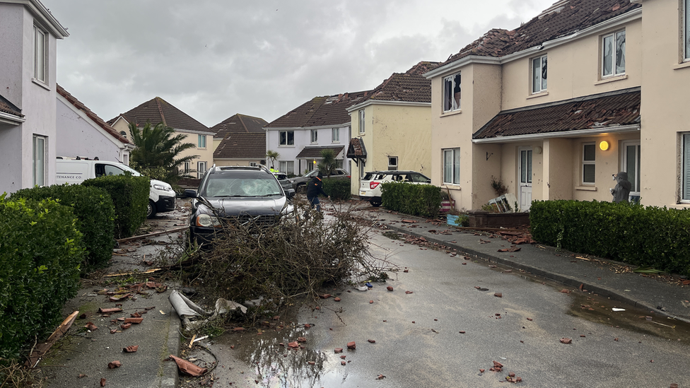 Photo of a street in Jersey with tiles missing from roofs with branches and debris all over the road.