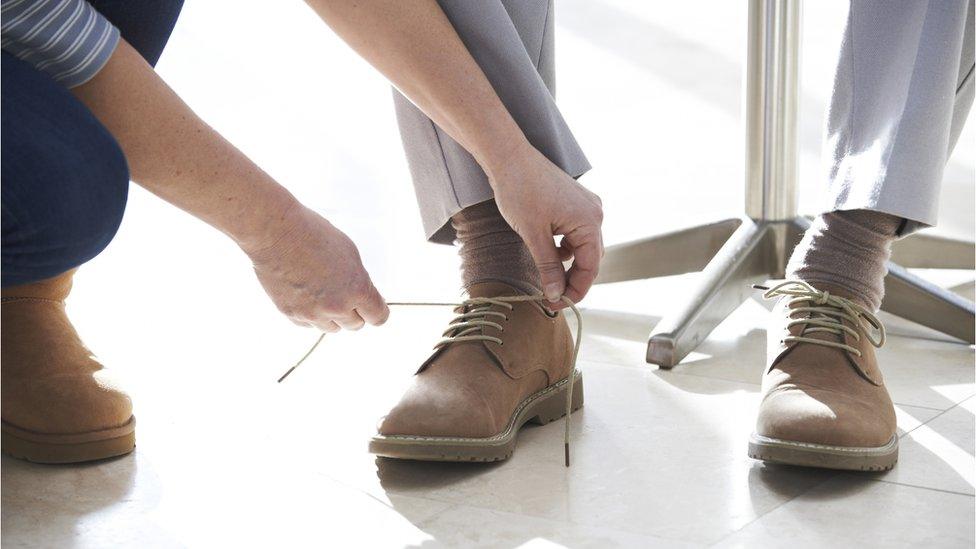 someone helping man tie shoe laces