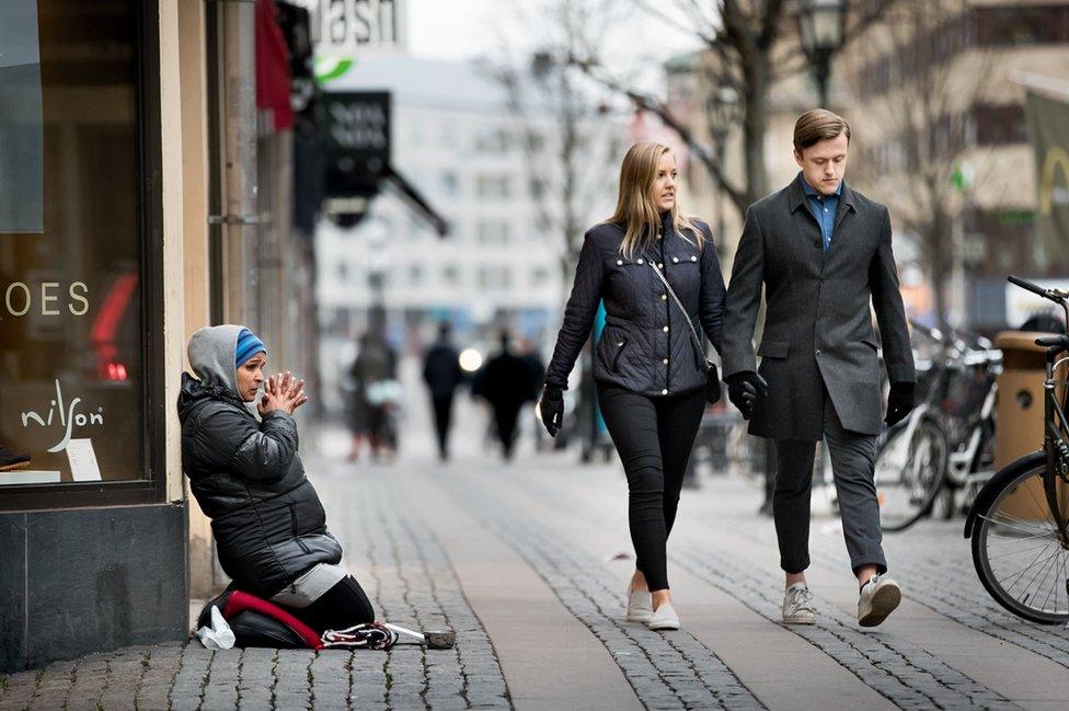 A woman begs as a smart couple walks past.