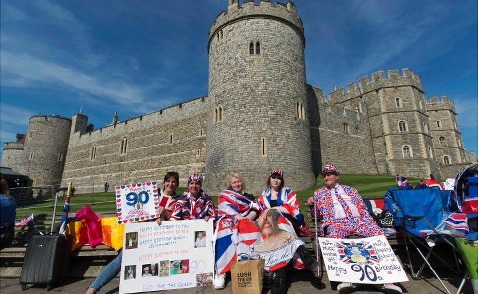 Royal well-wishers hold placards wishing Queen Elizabeth II a happy 90th birthday as they wait in hope of seeing her following her engagements in Windsor