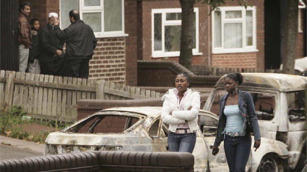 Local residents are seen near burnt out vehicles in Lozells on October 23, 2005 in Birmingham, England