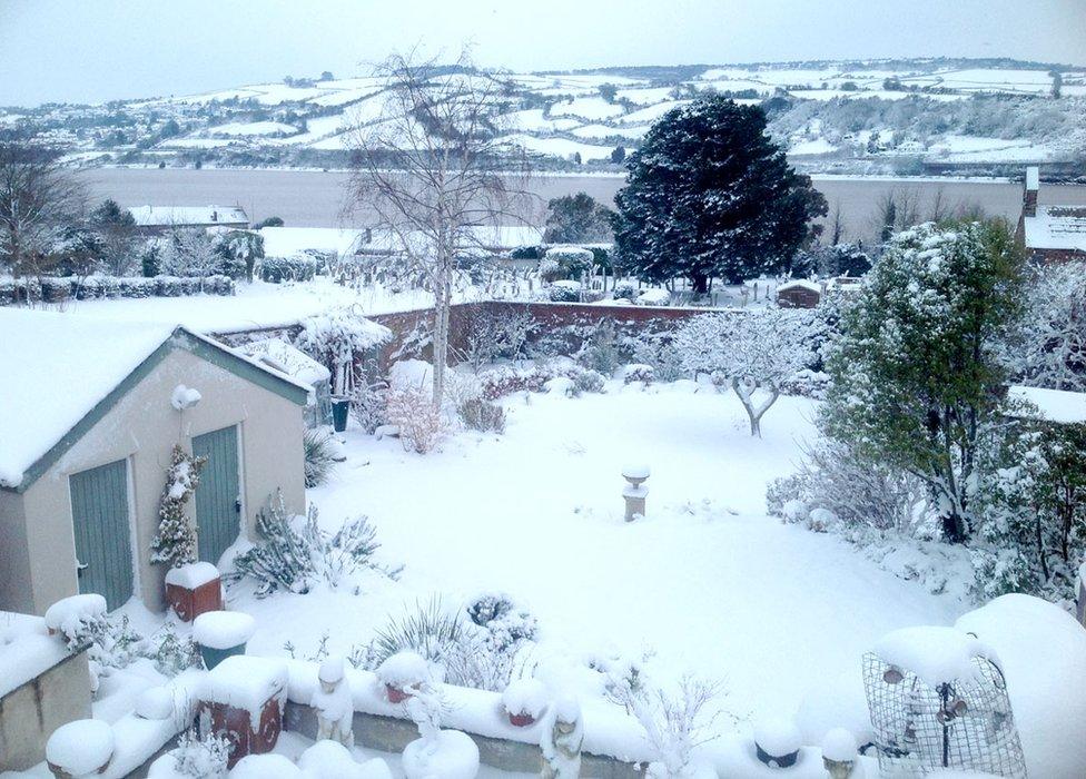 A garden covered in snow with rolling snow-covered hills in the background