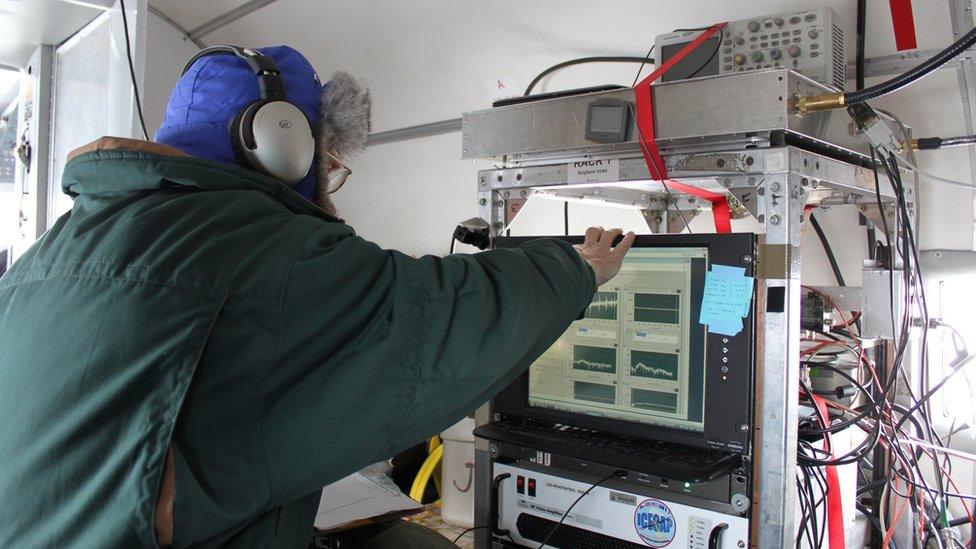 A scientist with their back turned, operating radar equipment aboard an aircraft