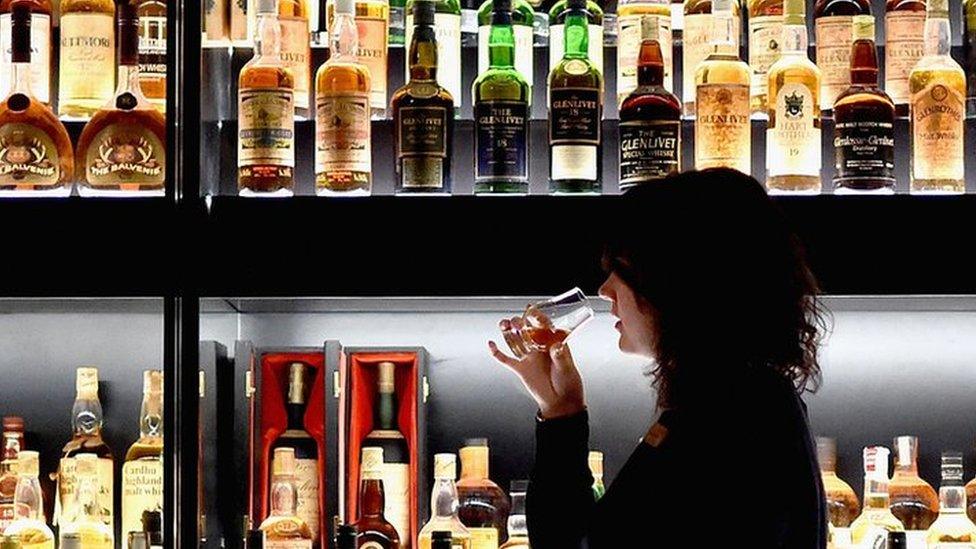 A glass of whisky being sampled against a backdrop of bottles